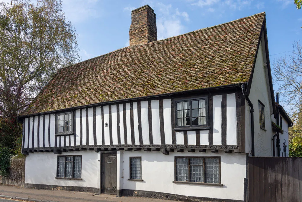 A historic half-timbered house with a steep, tiled roof and leaded windows on a sunny day.