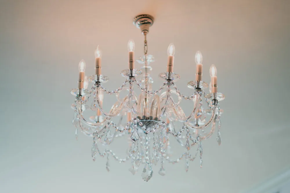 An ornate chandelier with crystal decorations and eight lit bulbs hangs from a ceiling.