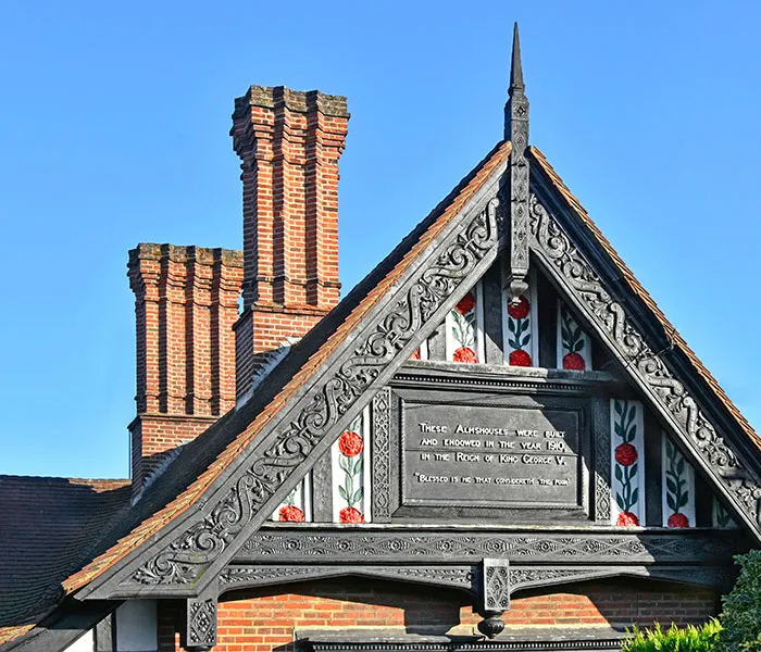 Ornate gable featuring Tudor-style architecture with an inscription panel under a clear blue sky, showing red floral accents.