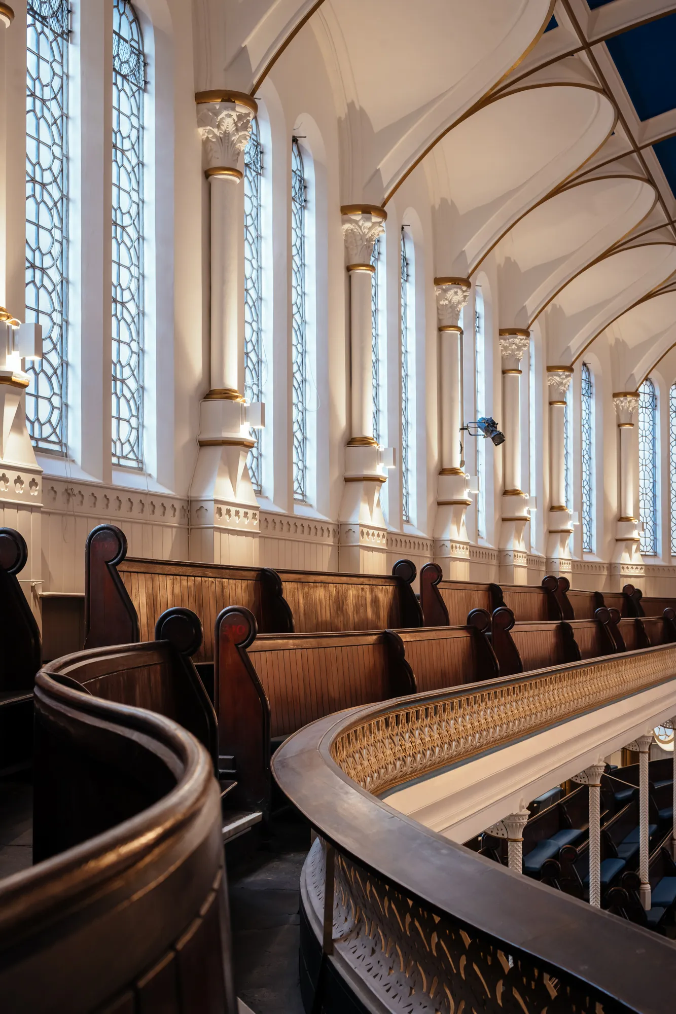 Interior view of a church with tall stained glass windows, arched ceilings, and wooden pews on the upper level.