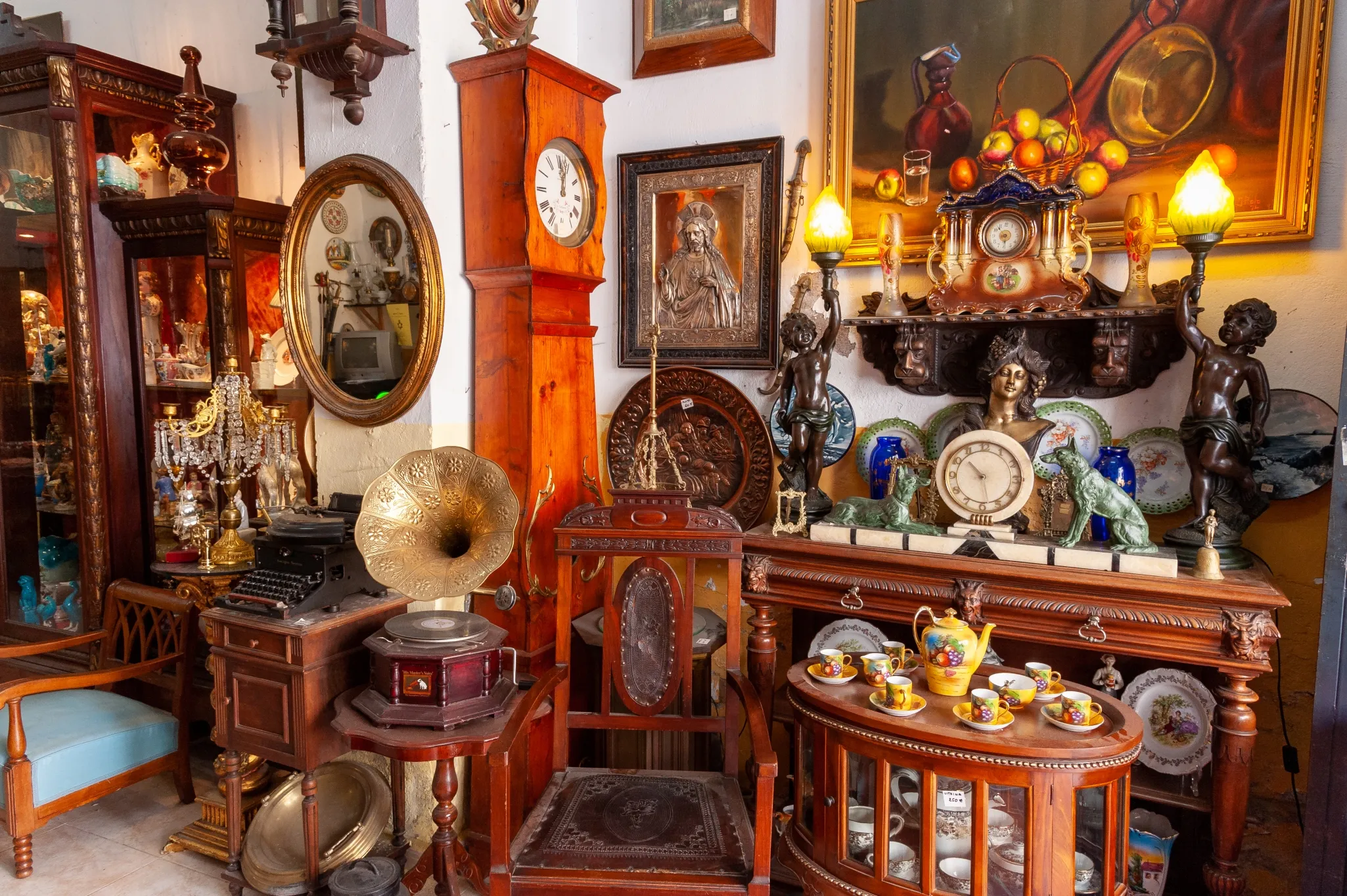 A cluttered antique shop with various vintage items including clocks, gramophones, paintings, and ornate furniture.