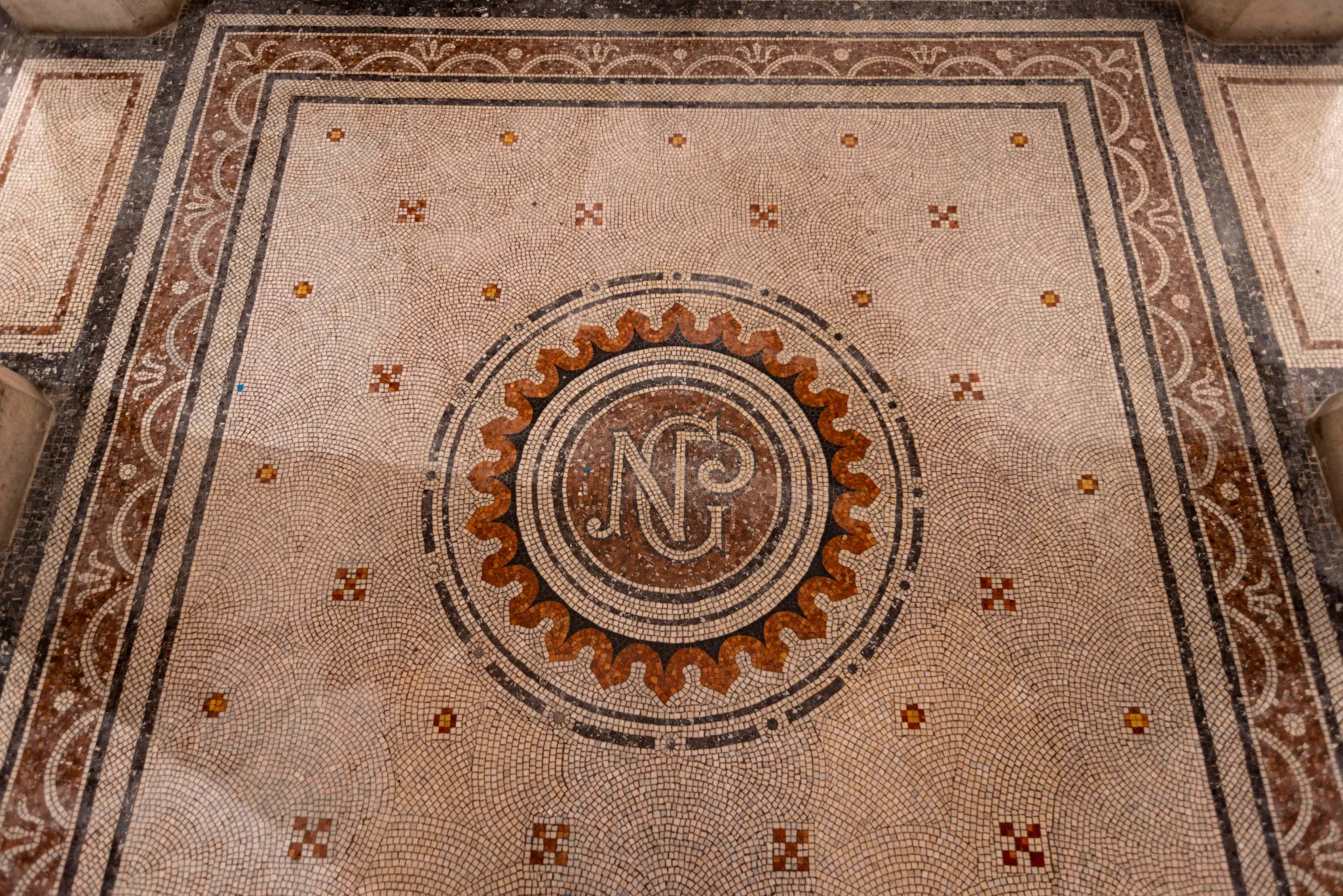 Intricate mosaic floor with a central circular design featuring the letters 