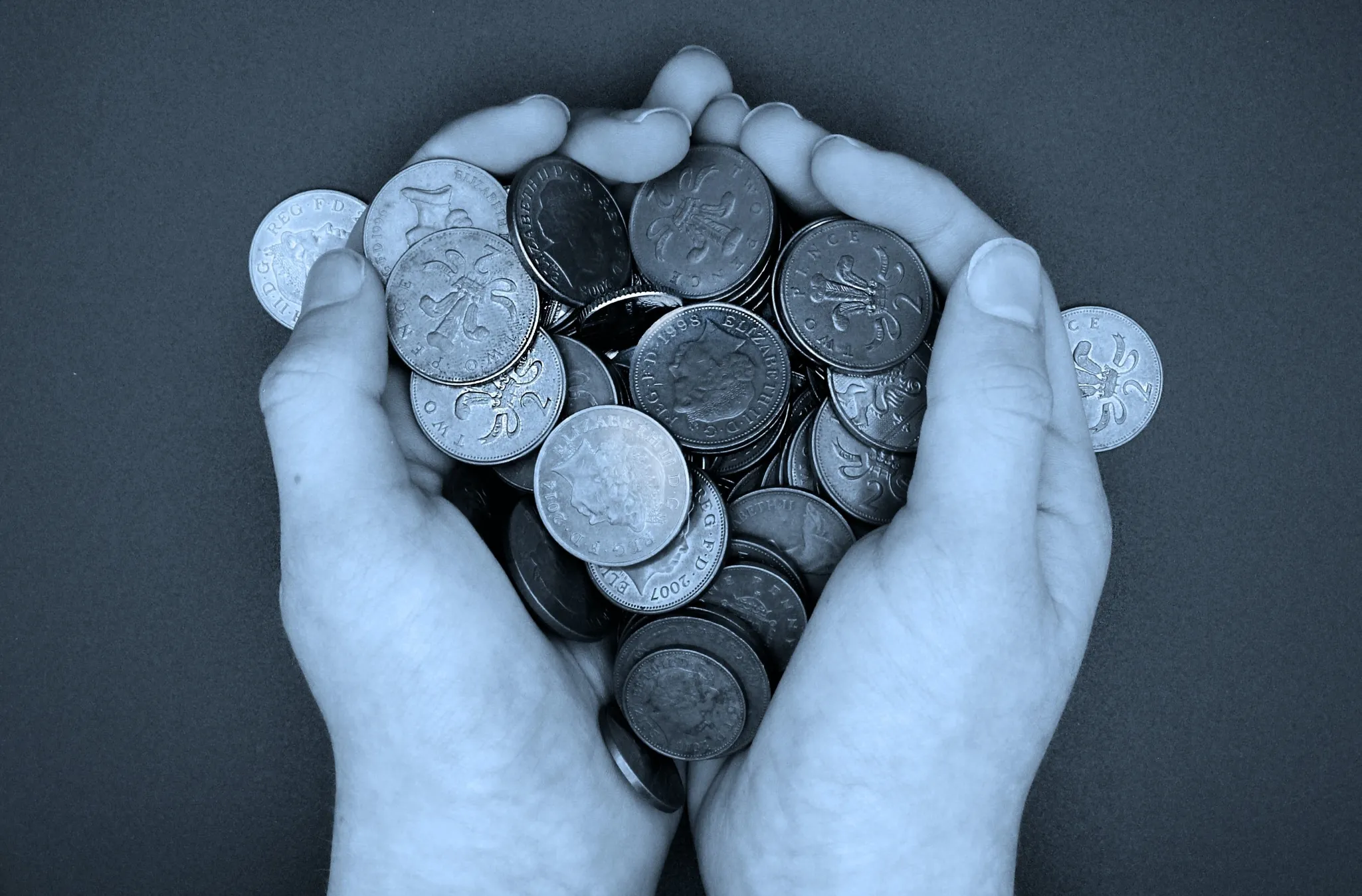 A pair of hands holding a collection of coins, some featuring different designs and engravings, against a neutral background.