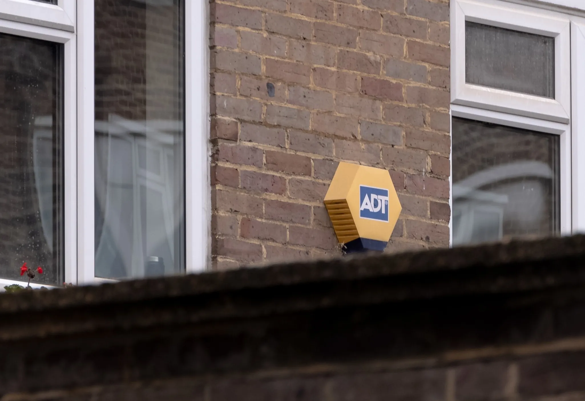 A yellow and blue ADT security system attached to the exterior brick wall of a building with windows.