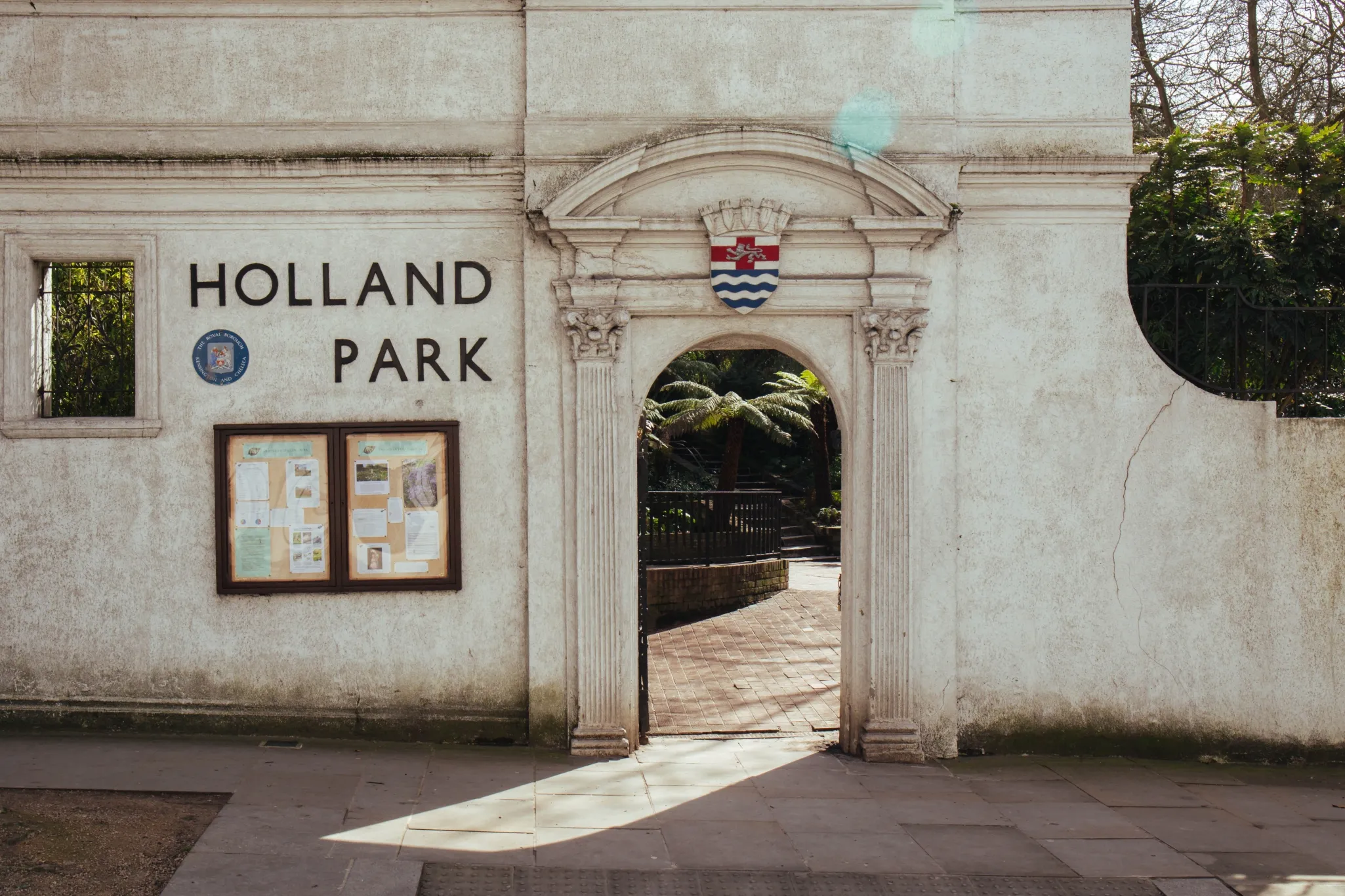 Entrance to Holland Park displaying a name sign, an information board, and a coat of arms above the arched doorway.