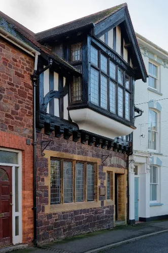 A street view of a historic two-story building with timber-framed windows on the upper floor and a brick and stone facade.