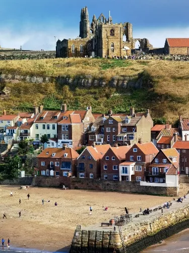 Coastal town with a sandy beach, residential buildings, and a historic cathedral atop a hill in the background.