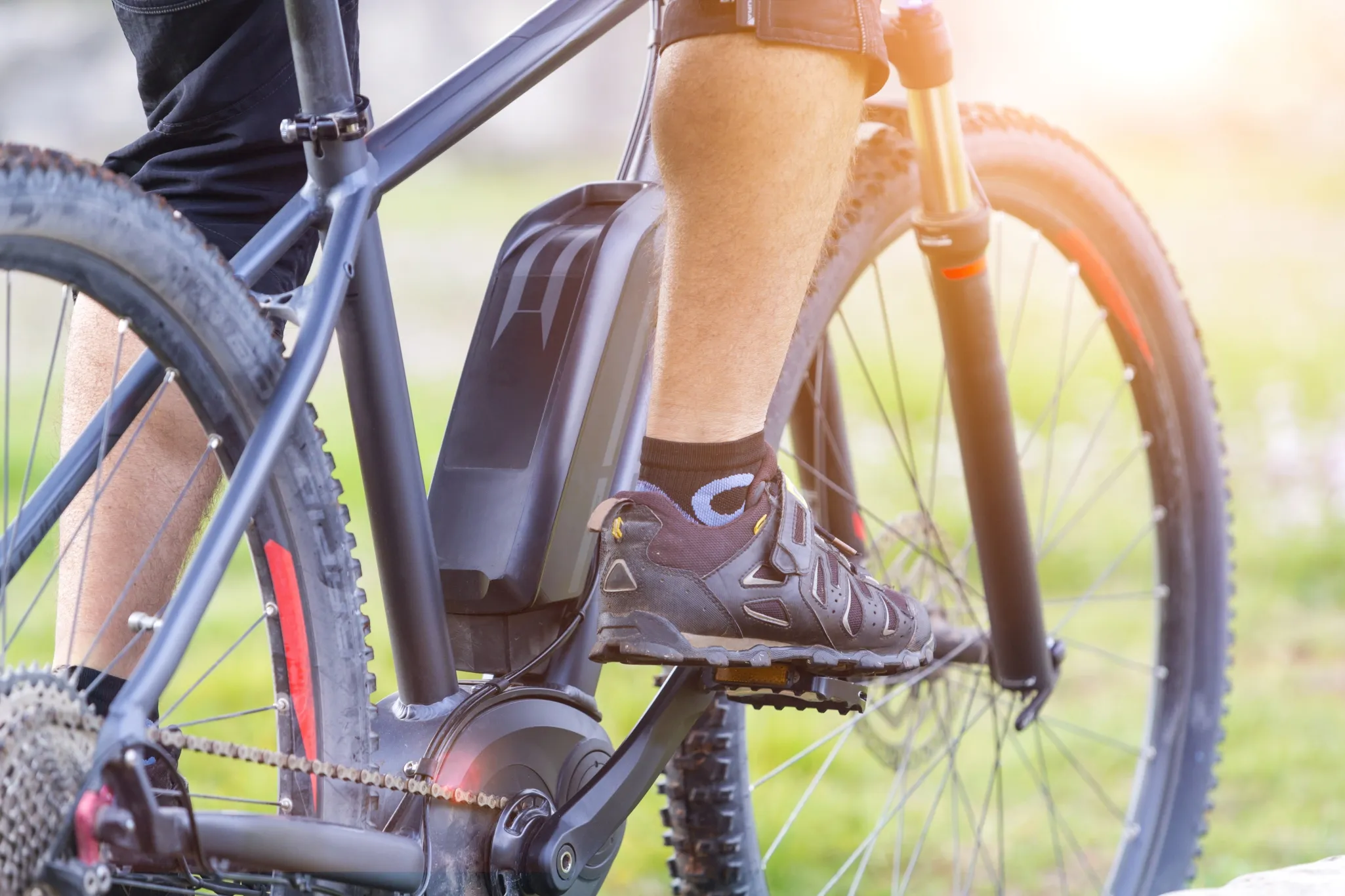 Close-up of a person riding an electric bike on a sunny day, focusing on the legs, bike frame, and electric motor.