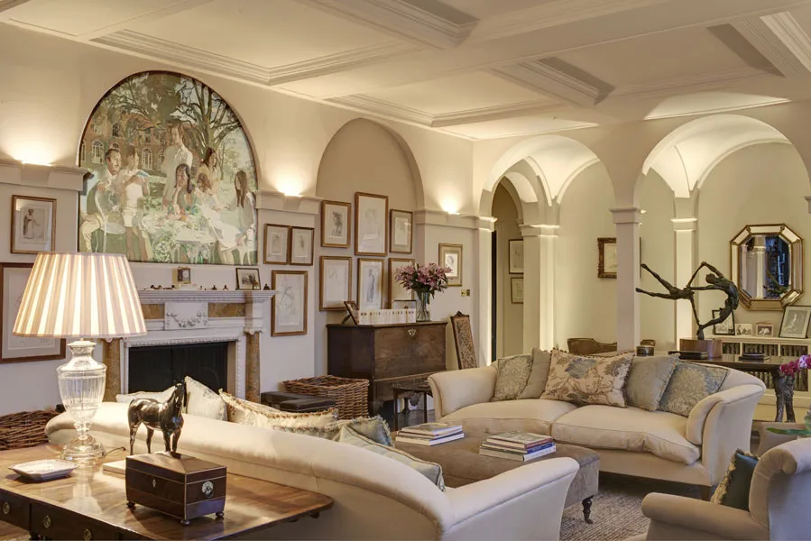 Elegant living room with arched doorways, beige sofas, a fireplace with art above, and various wall decorations and furniture.