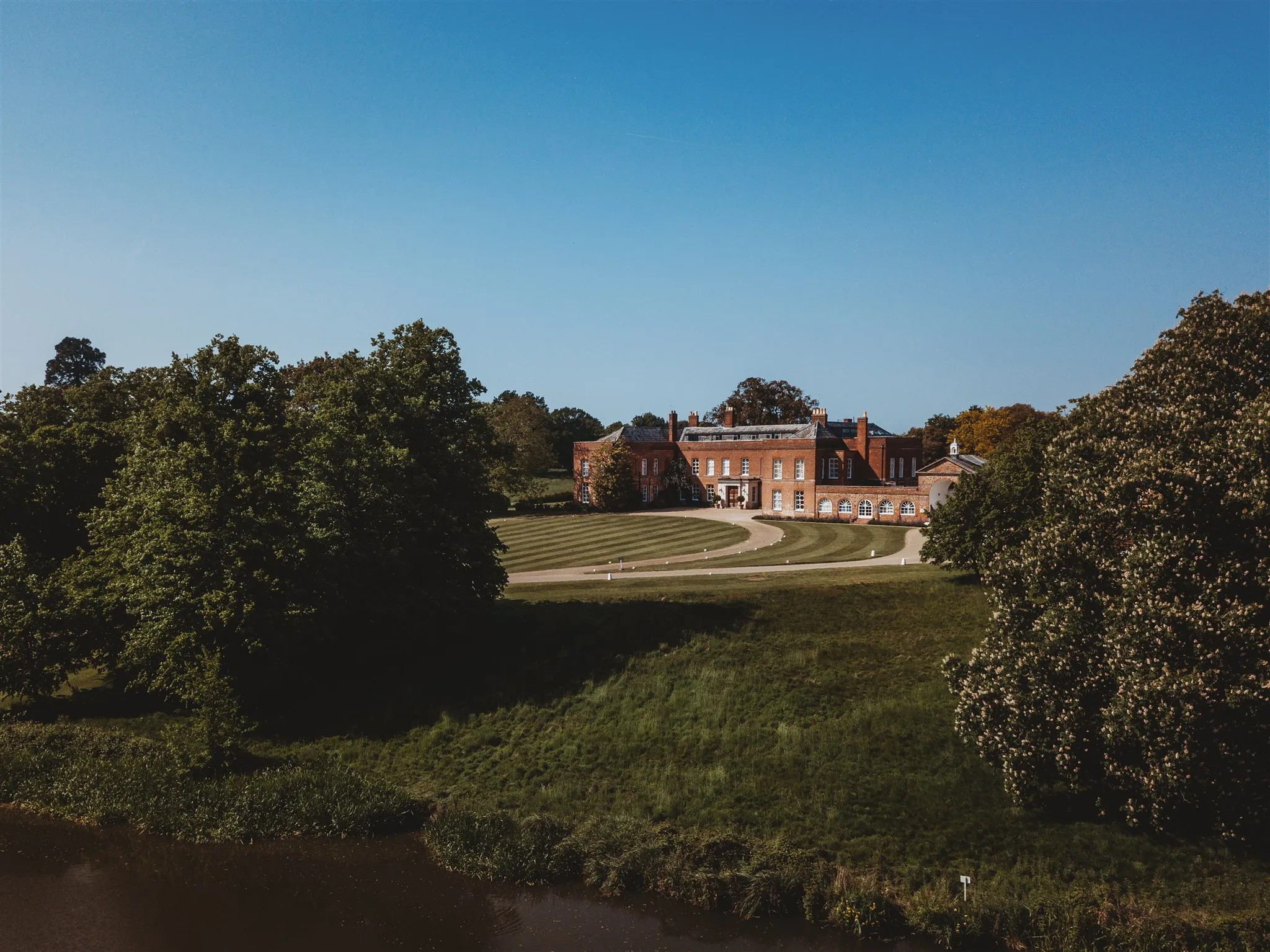 Braxted Park, historic red-brick manor house with a curved driveway is set amid, well-manicured lawns and trees.