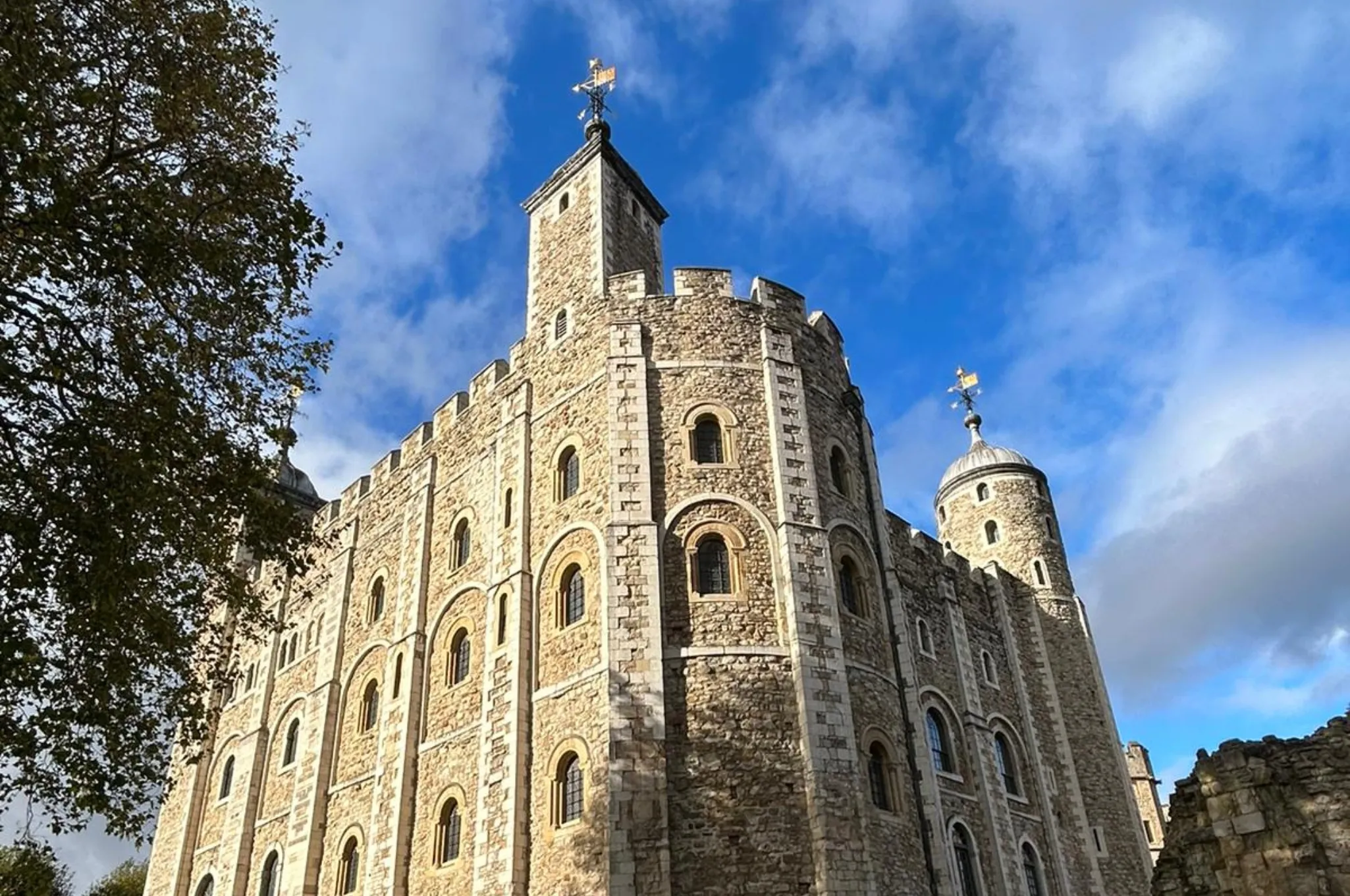 A stone fortress with crenellations and turrets under a partly cloudy sky, surrounded by trees.