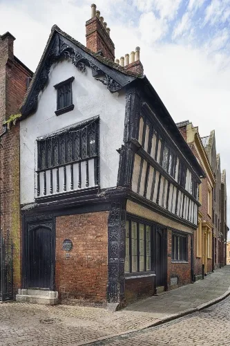 A narrow, two-story medieval timber-framed building with white and black facade on a cobblestone street.