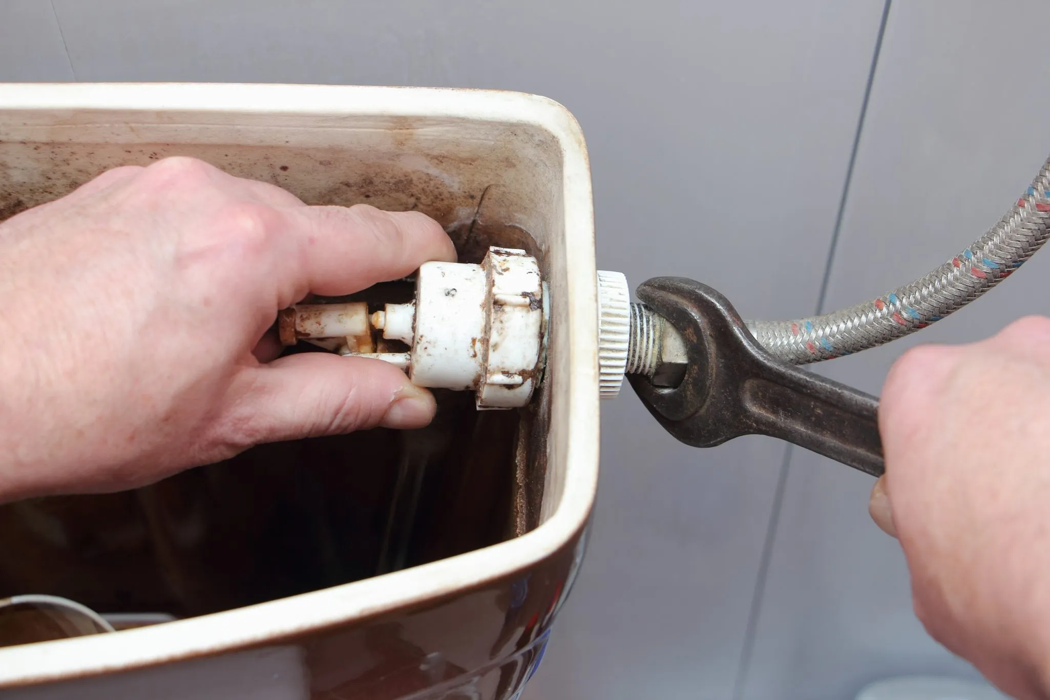 Hands using a wrench to tighten a fitting inside the tank of a toilet.