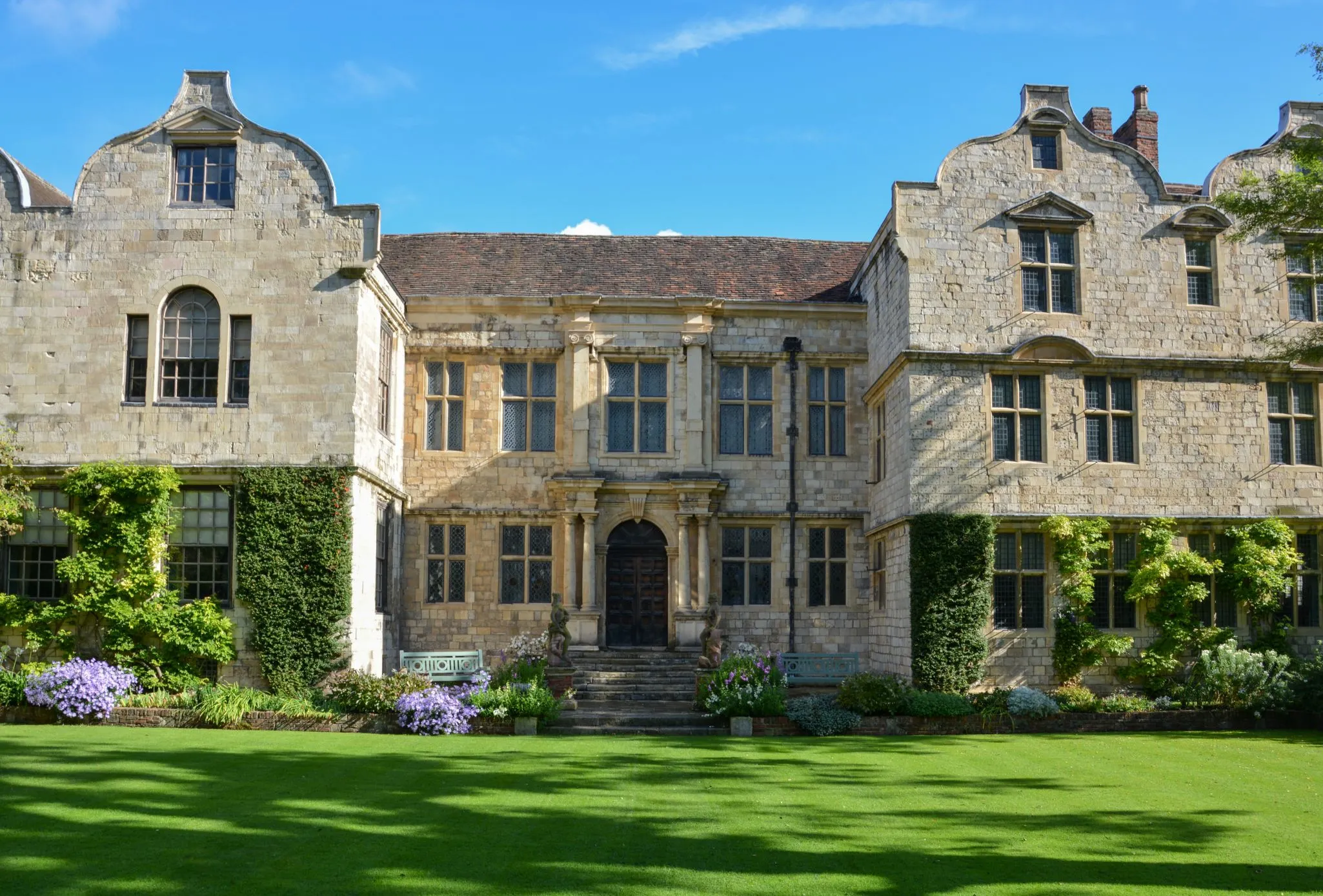 A large, historic stone building with an intricate facade and neatly manicured lawn on a clear, sunny day.