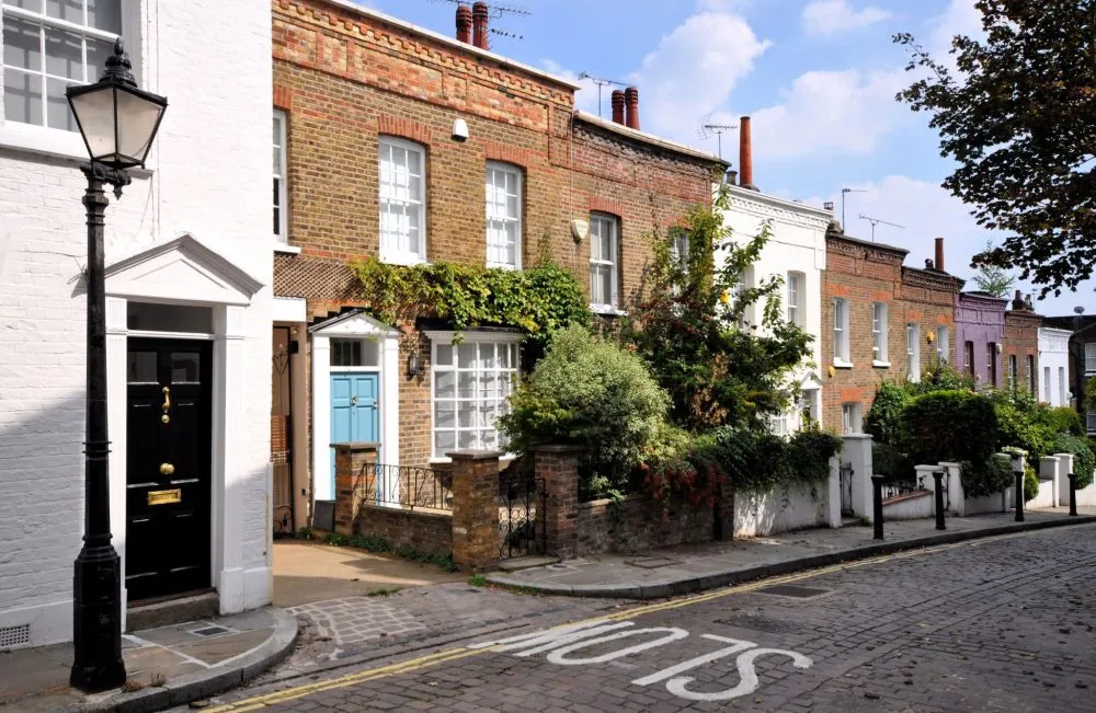 A row of charming terraced houses with brick and white facades, a black lamppost, and greenery along a cobblestone street.