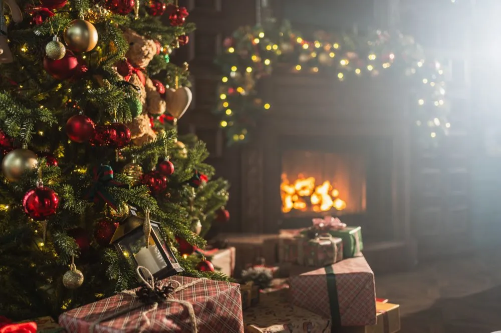 Cozy room with a decorated Christmas tree and wrapped gifts near a lit fireplace, adorned with garland and twinkling lights.