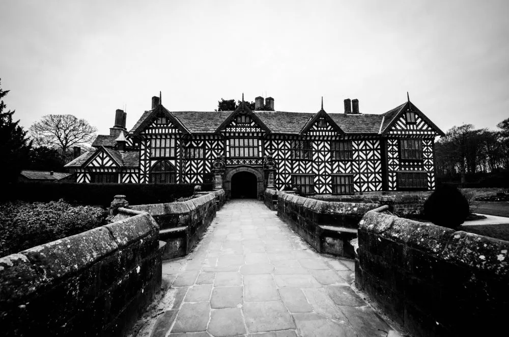 Black-and-white image of a historic half-timbered building with a stone walkway leading to the entrance.